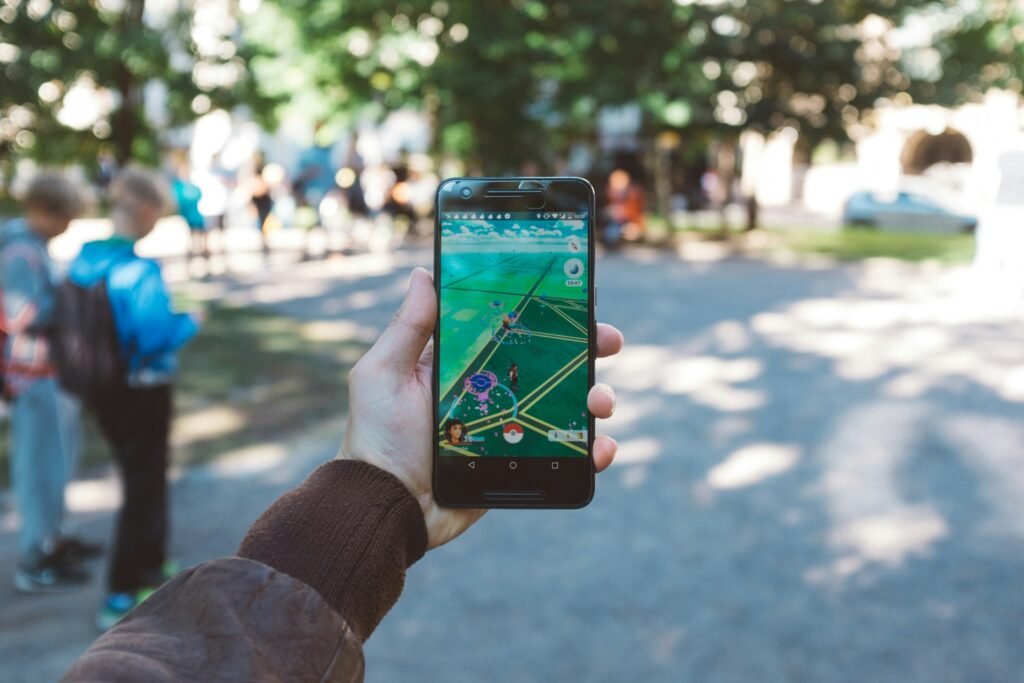 A person holding a smartphone at a park. The phone is has the Pokémon Go app on the screen.